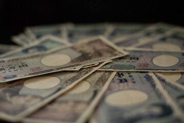 Blurred focus of pile of Japanese money in 1000 yen bills and 10000 yen bills on black background in soft focus