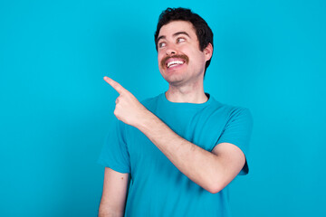 young handsome Caucasian man with moustache wearing blue t-shirt against blue background glad cheery demonstrating copy space look novelty