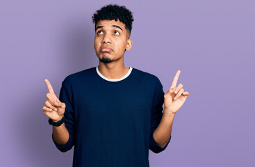 Young african american man wearing casual clothes pointing up looking sad and upset, indicating direction with fingers, unhappy and depressed.