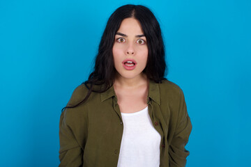 Obraz premium young beautiful tattooed girl standing against blue background having stunned and shocked look, with mouth open and jaw dropped exclaiming: Wow, I can't believe this. Surprise and shock