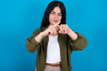young beautiful tattooed girl standing against blue background has rejection angry expression...