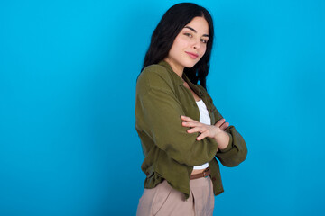 Image of cheerful young beautiful tattooed girl standing against blue background with arms crossed. Looking and smiling at the camera. Confidence concept.