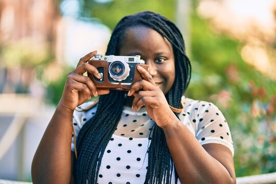 Young african american tourist woman smiling happy using vintage camera at the city.