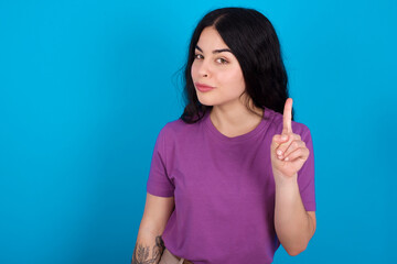 No sign gesture. Closeup portrait unhappy young beautiful tattooed girl wearing blue t-shirt raising fore finger up saying no. Negative emotions facial expressions, feelings.