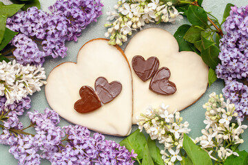 Obraz na płótnie Canvas Gingerbread covered with chocolate glaze in the form of a heart in a frame of flowering lilac. Top View