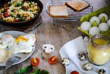 Couscous with vegetables cooked in a pan, toast and fried eggs on the table.
