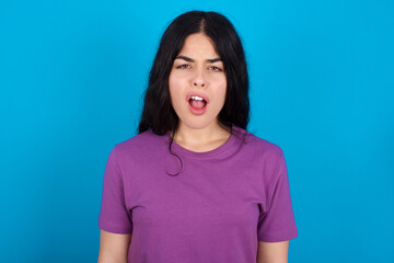 Fototapeta premium young beautiful tattooed girl wearing blue t-shirt standing against blue background yawns with opened mouth stands. Daily morning routine