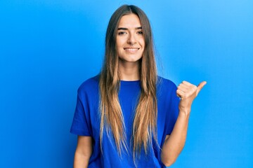 Fototapeta premium Young hispanic woman wearing casual clothes smiling with happy face looking and pointing to the side with thumb up.