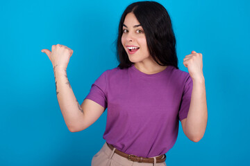 Hooray cool young beautiful tattooed girl wearing blue t-shirt standing against blue background point back empty space hand fist