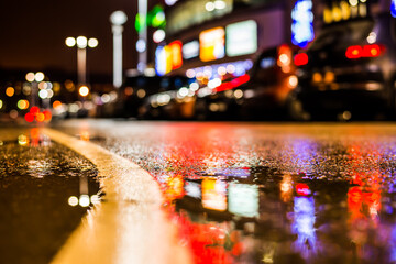 Rainy night in the parking shopping mall, parked cars and marking the line going into the distance. Close up view of a puddle on the level of the dividing line
