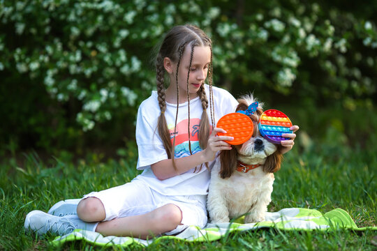 Creative Image With Child Playing Poppit Fidget Toy. Young Girl At  Holding Pop It New Fidget Toy, Popular With Kids, Helps Them To Concentrate. Girl on the lawn with a dog playing antistress