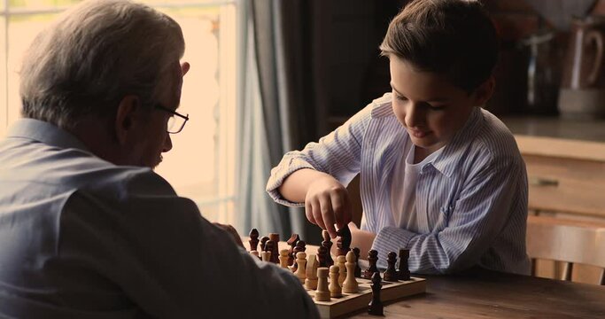 Grandpa and little grandson play chess sit at table. Multi-generational family engaged in educational board game. Kid development, improve concentration, gain abstract thinking skills, hobby concept