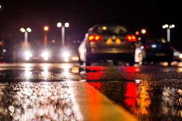 Rainy night in the parking shopping mall, the headlights of the cars. Close up view from the level of the dividing line