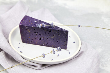 Piece of lavender cheese with dry basil and lavender flowers in plate on concrete table