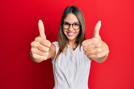 Young brunette woman wearing casual clothes and glasses approving doing positive gesture with hand, thumbs up smiling and happy for success. winner gesture.