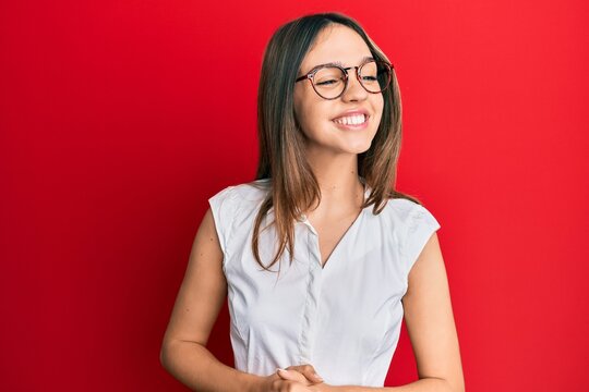 Young brunette woman wearing casual clothes and glasses looking away to side with smile on face, natural expression. laughing confident.