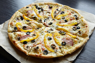Round pizza with chesse, ham, yellow bell pepper, olives and mushrooms on wooden table