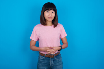 Business Concept - Portrait of young beautiful asian woman wearing pink t-shirt against blue wall holding hands with confident face.