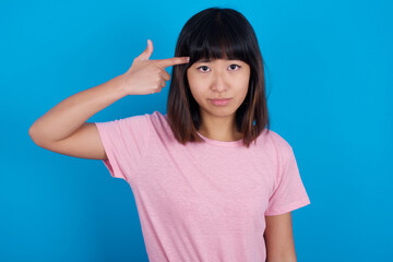 Unhappy young beautiful asian woman wearing pink t-shirt against blue wall curves lips and makes...