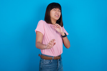 Ugh how disgusting! Displeased Young beautiful asian girl wearing pink t-shirt against blue background, has dissatisfied facial expression as sees something abominable.