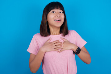 Happy smiling Young beautiful asian girl wearing pink t-shirt against blue background has hands on...
