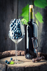 Red wine in bottle and dark grapes on wooden barrel.