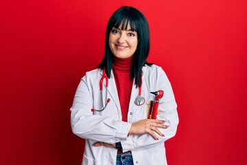 Young hispanic woman wearing doctor uniform and stethoscope happy face smiling with crossed arms looking at the camera. positive person.