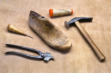 Boot maker tools. Cobbler equipment on leather underlay. Fittings for shoemakers. Awl, straight last, cobbler's hammer, cordwainer's stitch with needle, pliers.