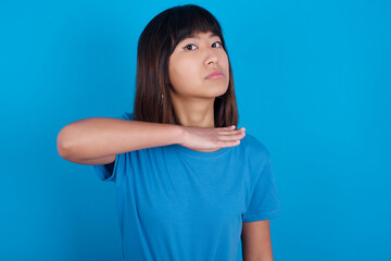 young beautiful asian girl wearing blue t-shirt against blue background cutting throat with hand as...