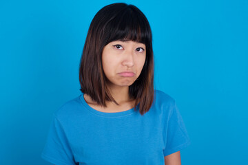 Fototapeta premium young beautiful asian girl wearing blue t-shirt against blue background depressed and worry for distress, crying angry and afraid. Sad expression.