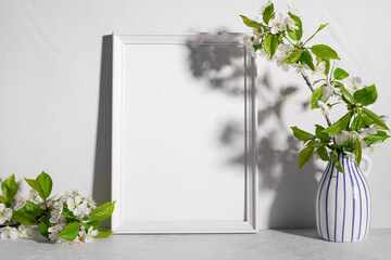 blank postcard frame mockup with cherry tree blossoms in vase on table in sunlight. template for lettering, text or design