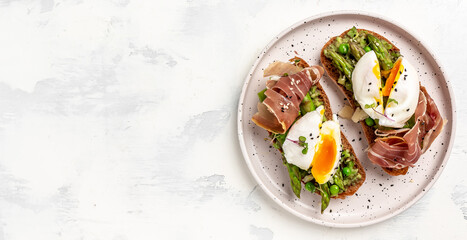 toasts with avocado, asparagus and Benedict Poached eggs with prosciutto on white plate, top view, Long banner format, top view