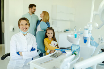 Fototapeta premium girl sitting in dental chair and smiling young kind female dentist in white coat looking at camera.
