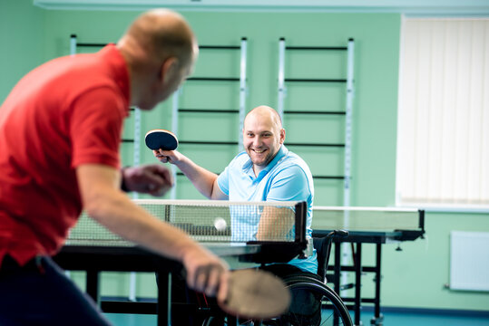 Adult disabled man in a wheelchair play at table tennis with his coach - Powered by Adobe