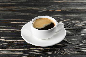 White cup with espresso coffee on a black wooden background.