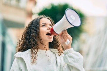 Hispanic child girl shouting angry using megaphone at the city. - obrazy, fototapety, plakaty