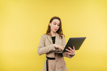 Business beautiful woman with laptop isolated on a colored background. Concentrated attractive freelancer woman in suit working on laptop on yellow wall background with serious face.