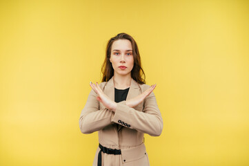 Beautiful woman in a beige jacket shows a stop gesture with arms crossed and looks at the camera with a serious face.