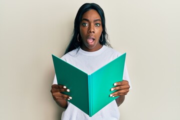 Young african american woman reading book afraid and shocked with surprise and amazed expression, fear and excited face.