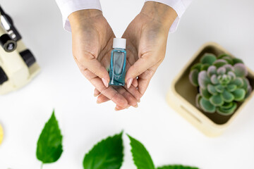 Close-up hands hold cosmetic bottle with water-tonic on white lab background with microscope out of...