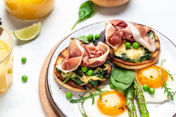 Delicious fresh breakfast served grilled bun with spinach and cheese, asparagus, jamon, ham, prosciutto and fried egg. fresh juice, Balanced diet. place for text, top view