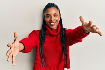 African american woman wearing casual winter sweater looking at the camera smiling with open arms for hug. cheerful expression embracing happiness.