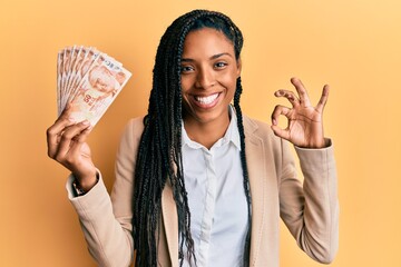 African american woman with braids holding 50 turkish lira banknotes doing ok sign with fingers,...