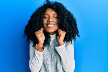 African american woman with afro hair wearing casual winter sweater excited for success with arms raised and eyes closed celebrating victory smiling. winner concept.