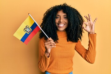 African american woman with afro hair holding ecuador flag doing ok sign with fingers, smiling friendly gesturing excellent symbol