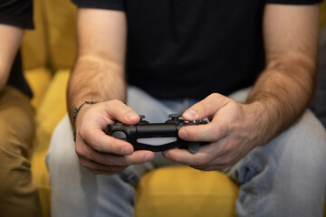 Hairy male gamer hands holding remote joystick close up. two guys intently Enjoying video game. man Playing Videogame sitting on comfy yellow sofa Resting At Home. Fans together, fun for two