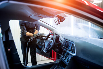 Naklejka premium Car service worker cleans interiror with steam cleaner