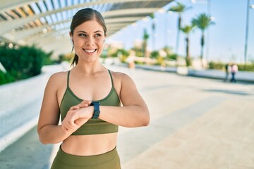 Young blonde sportswoman wearing sportswear touching watch at the city.