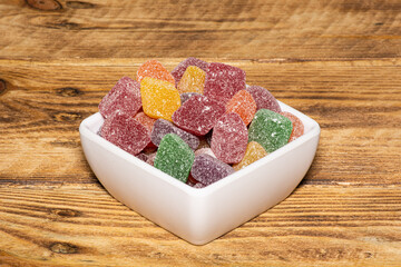 Bowl of sweet colorful sugar rich jubes. Candy bowl isolated on wood grain background.