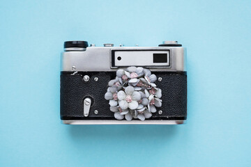Retro film camera with textile flowers instead of a lens. Frame concept on light blue background.